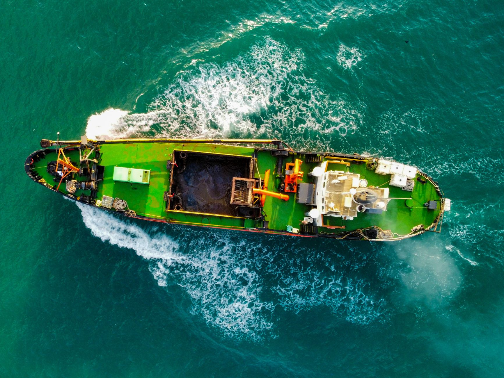 Drone shot capturing a cargo ship navigating through the vibrant turquoise ocean waters.