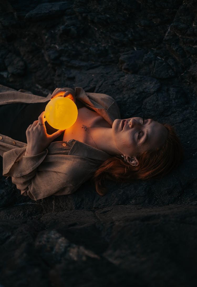 Woman Lying On Her Back With Her Eyes Closed Holding A Glowing Orb