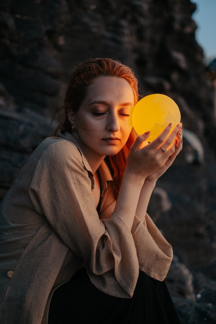 Woman Sitting With Her Eyes Closed Holding A Glowing Orb In Her Hands