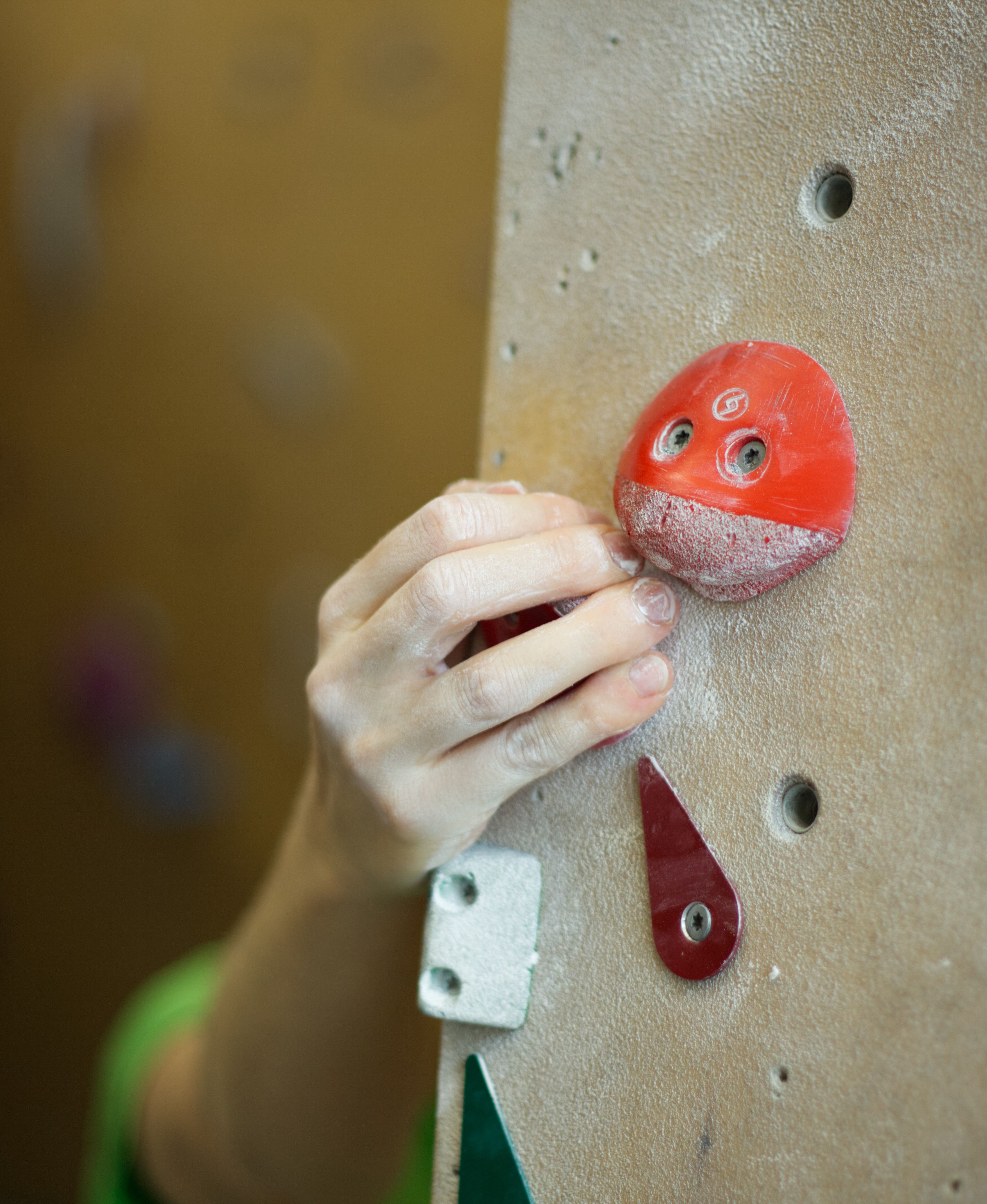 A hand grasping a red climbing hold on an indoor rock wall, showcasing sport and technique.