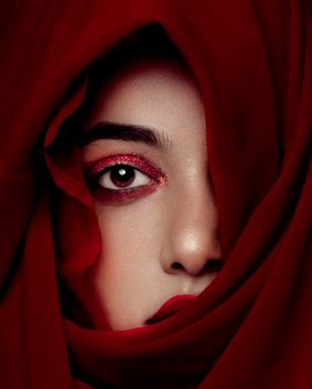 Close-up portrait of a woman's face partially covered by a flowing red veil, exuding mystery.