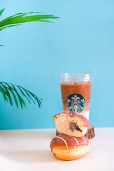 Delicious iced coffee with a bitten chocolate-filled doughnut against a light blue backdrop.