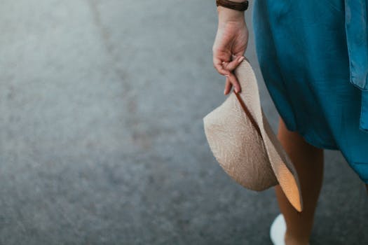 Close-up of a woman holding a straw hat, wearing a blue dress, capturing a relaxed summer day.
