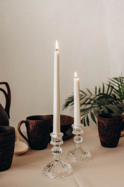 A warm dining scene with tall lit candles and rustic ceramic mugs on a table.