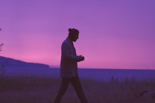Silhouette of a person walking on a beach at purple sunset in Jönköping, Sweden.