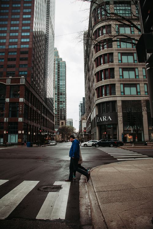 Free A person crossing a street in Chicago's urban landscape, surrounded by tall buildings. Stock Photo
