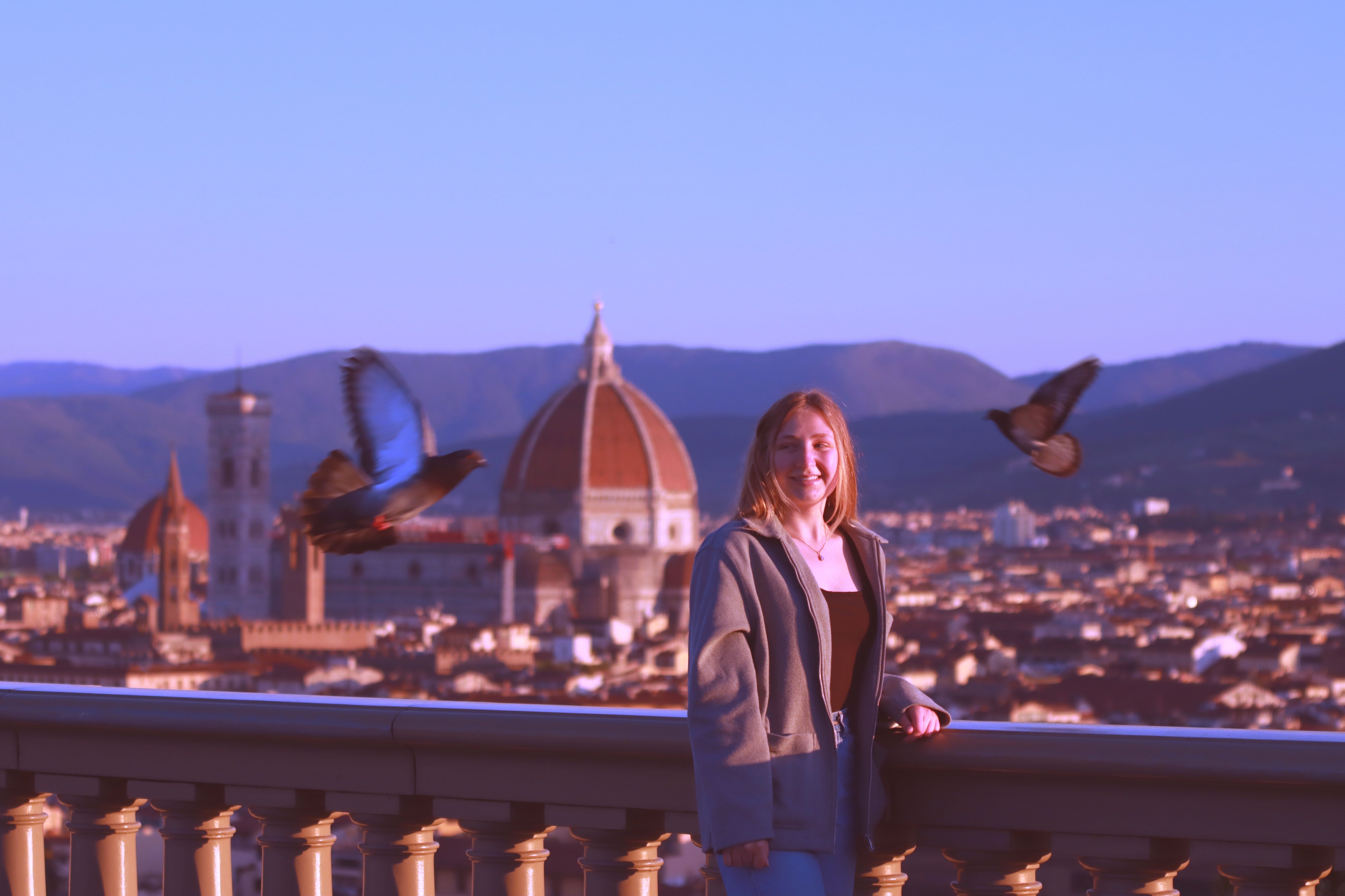 Woman enjoys panoramic view of Florence from Piazzale Michelangelo with pigeons flying by.