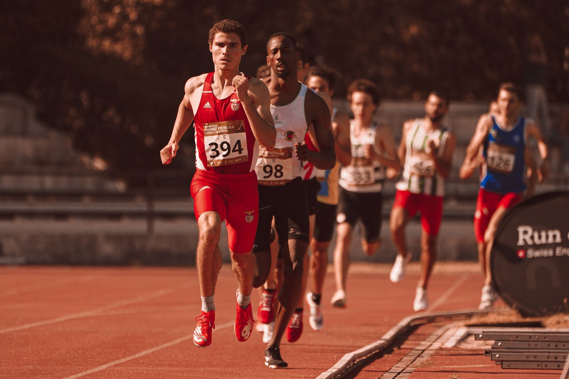 Groep atleten die deelnemen aan een atletiekwedstrijd op een buitensportbaan onder zonlicht.