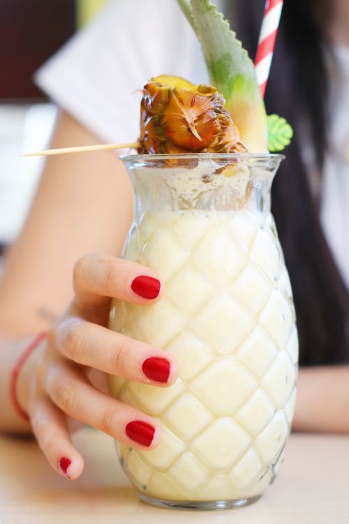 Free Close-up of a pineapple smoothie in a glass held by a woman with red nails. Perfect for summer. Stock Photo