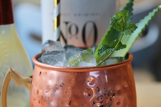 Close-up of a cold cocktail in a copper mug with ice, mint, and straw.