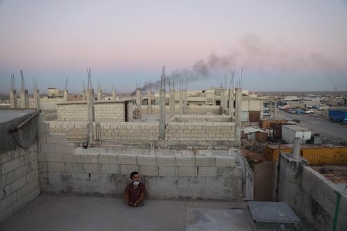 Free A lone man sits amid unfinished buildings in Syria during twilight, highlighting urban resilience. Stock Photo