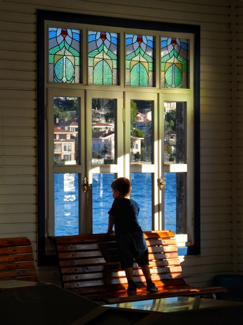 Free A child looks out through a vibrant stained glass window with a scenic waterfront view. Stock Photo