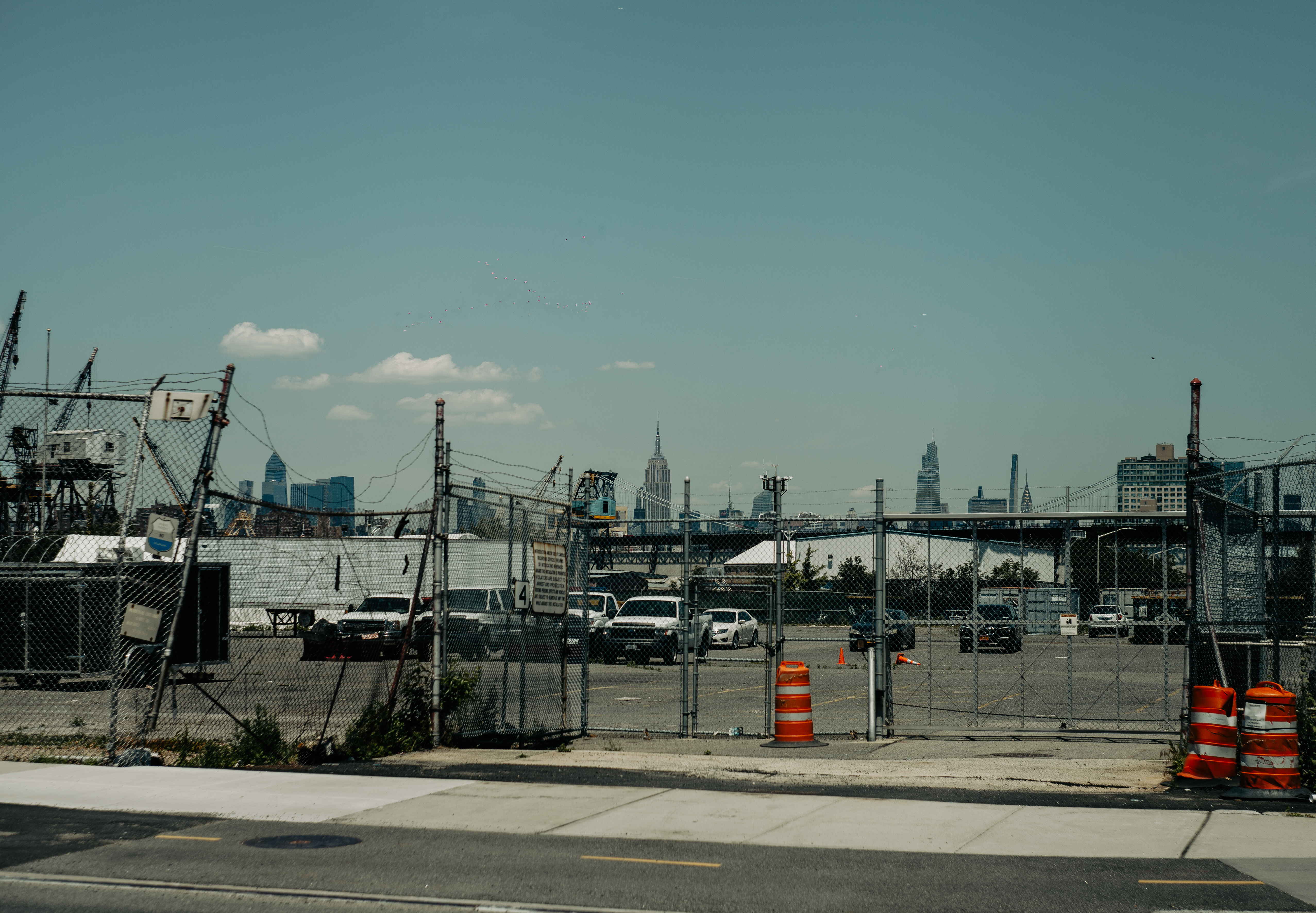 Parking lot with chain link fence and New York City skyline in view from a distance.