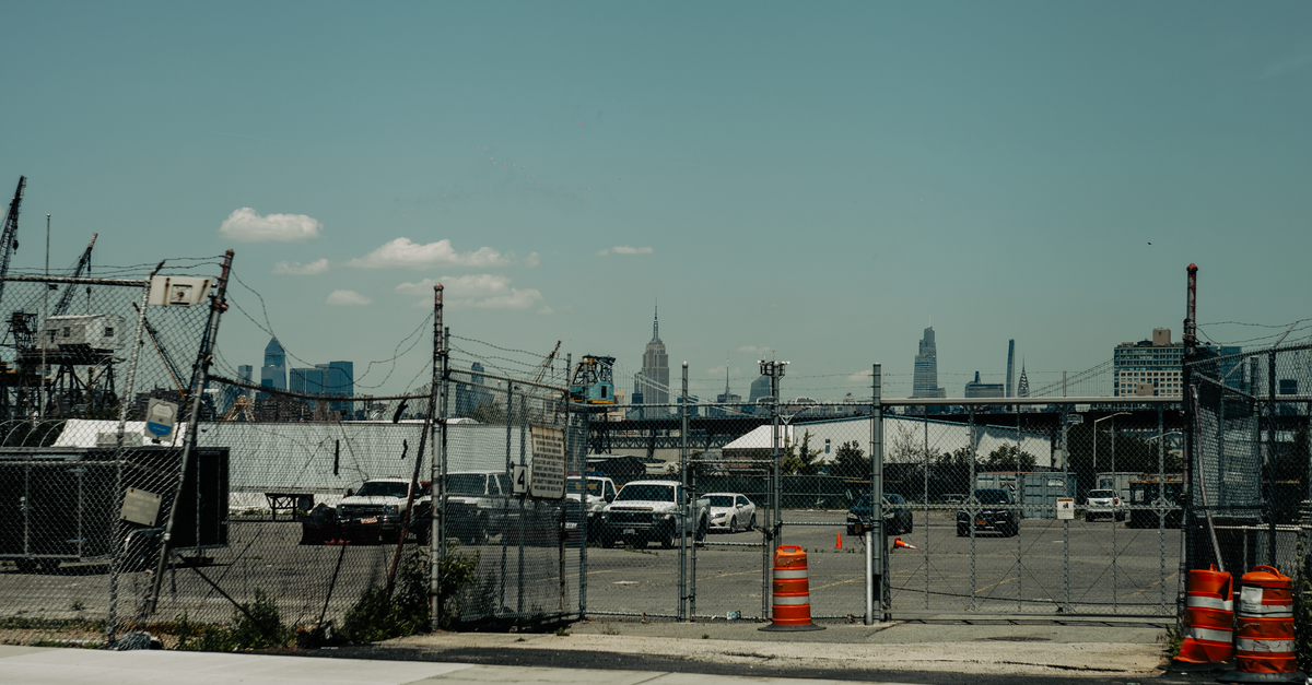 Parking lot with chain link fence and New York City skyline in view from a distance.