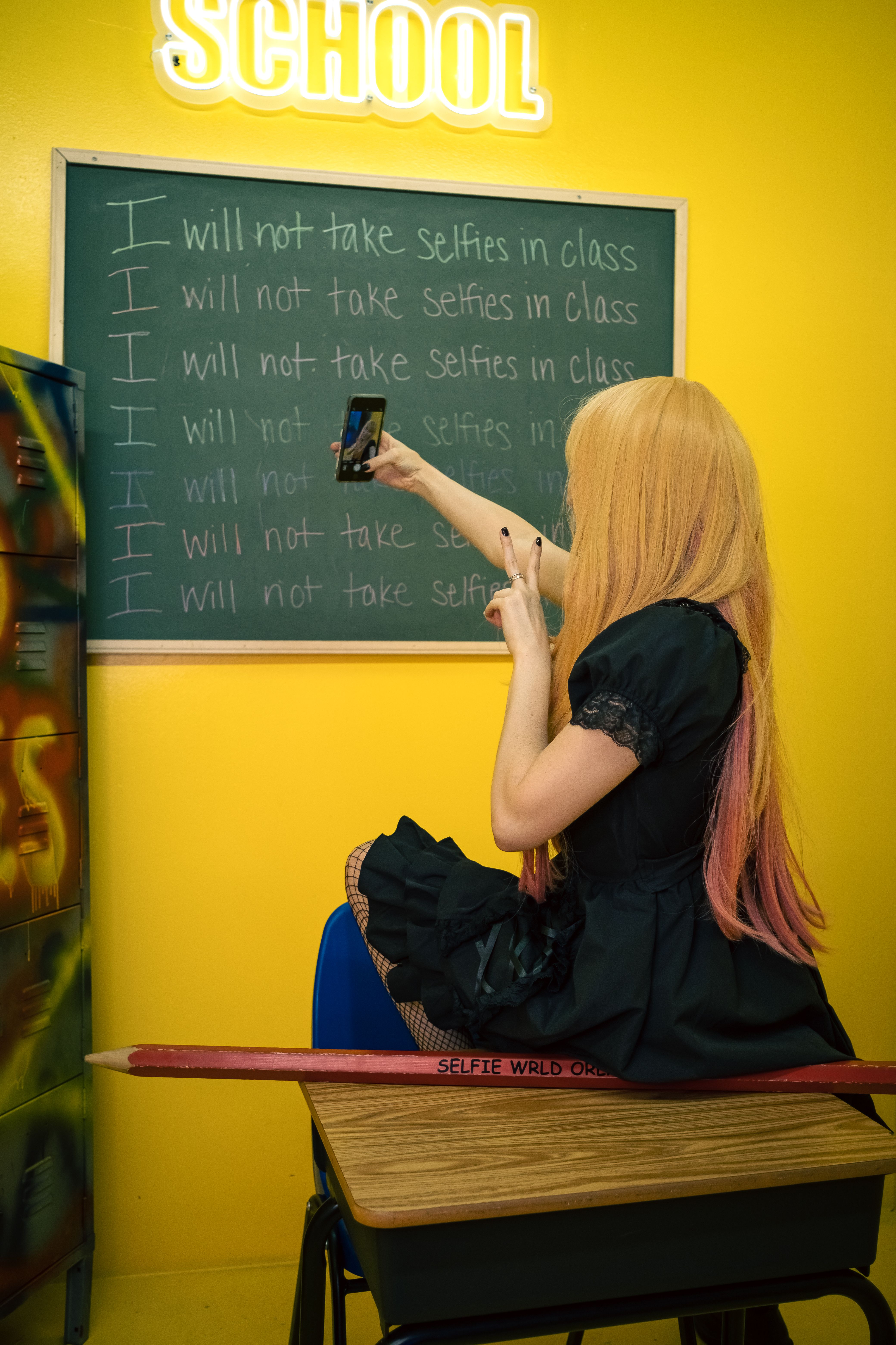 Woman taking a selfie in a vibrant classroom, with humor on not taking selfies in class.
