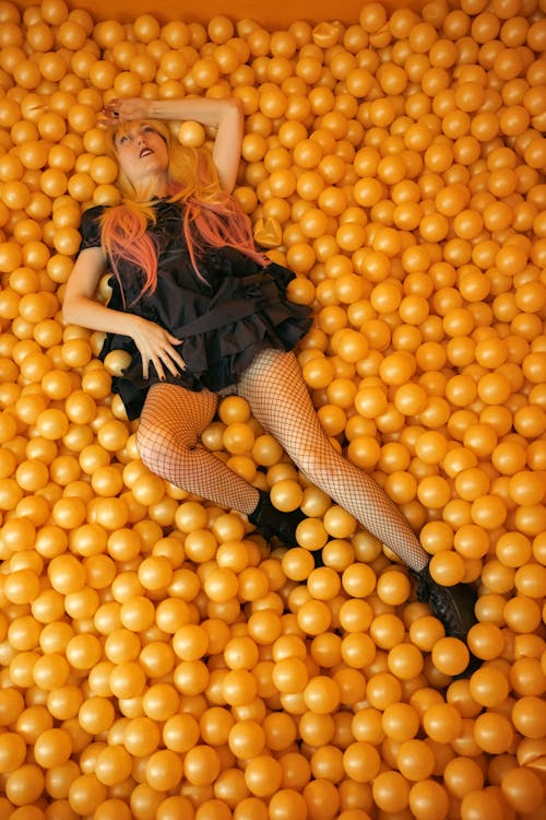 Woman in Black Dress Lying on Yellow Round Balls