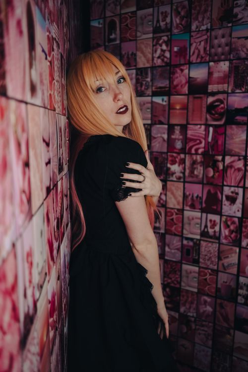 Free A fashionable redhead woman in a black dress poses against a vibrant, artistic wall. Stock Photo
