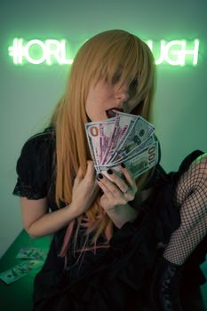 A person in black attire holds dollar bills in a neon-lit room.