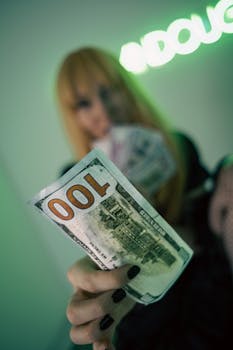 Dramatic shot capturing a hand holding a prominently displayed hundred dollar bill with a blurred background.