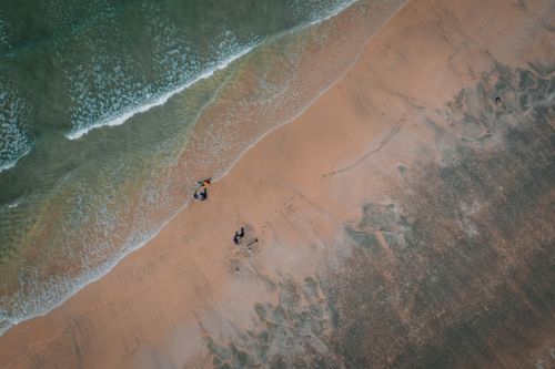Free Drone shot of a tranquil beach with waves lapping the shore and a few people walking. Stock Photo