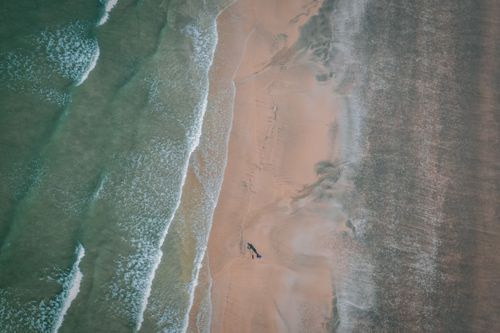 Free Drone-captured scenic image of tranquil beach waves meeting a vast sandy shore, ideal for nature lovers. Stock Photo
