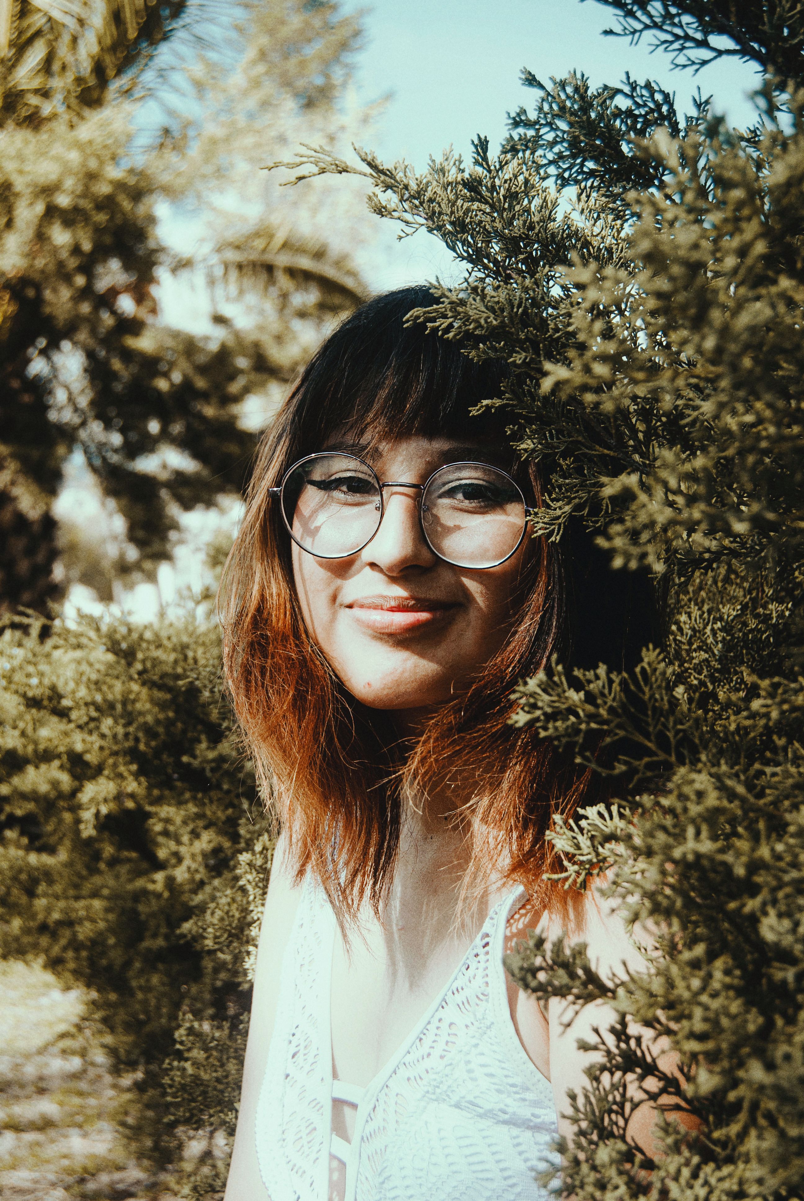 Jeune femme souriante portant des lunettes de vue, au milieu de la verdure