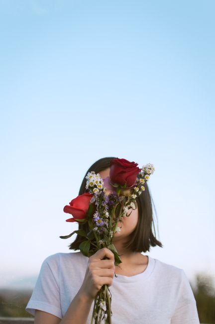 A teenager with straight hair holds colorful flowers, obscuring her face against a clear sky in Mexico City.