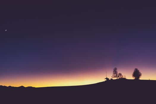 Silhouette of trees and moon against a twilight gradient at Irschenberg, Bavaria.