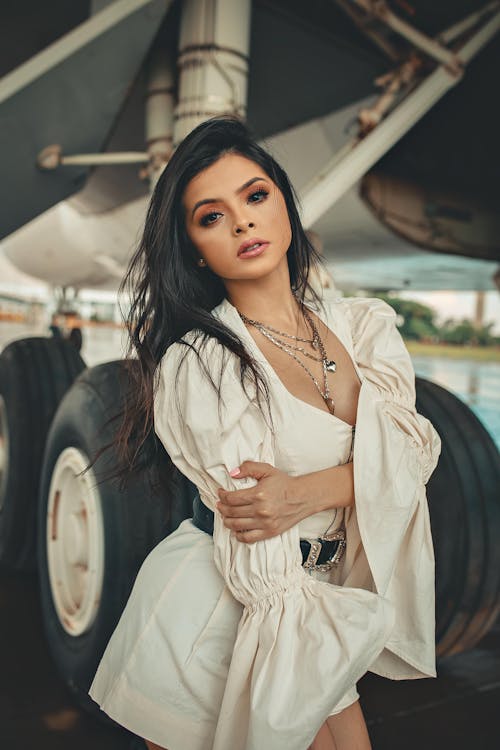 Woman in White Dress Posing Near Airplane Landing Gears