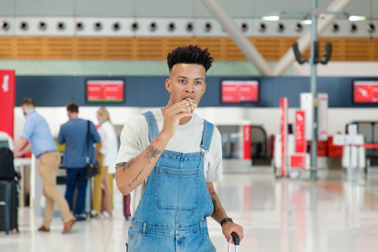 A Man In A Denim Overall Eating A Cookie At An Airport