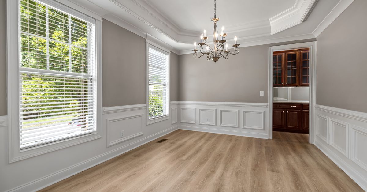 Spacious empty dining room with elegant chandelier, large windows, and wooden floors.