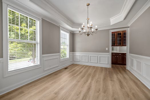 Spacious empty dining room with elegant chandelier, large windows, and wooden floors.