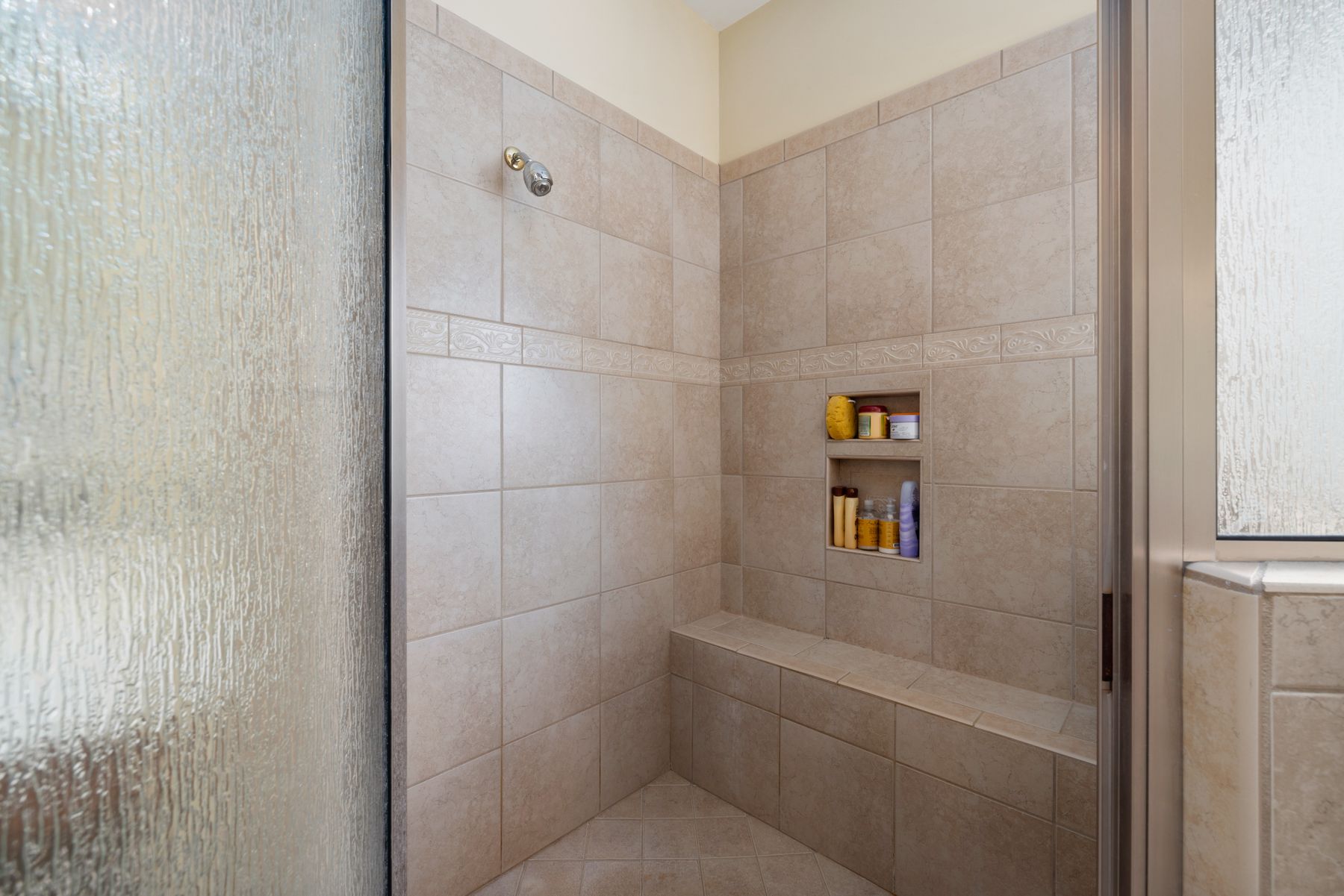 Walk-in shower with glass enclosure, built-in niches, bench, and warm neutral tile