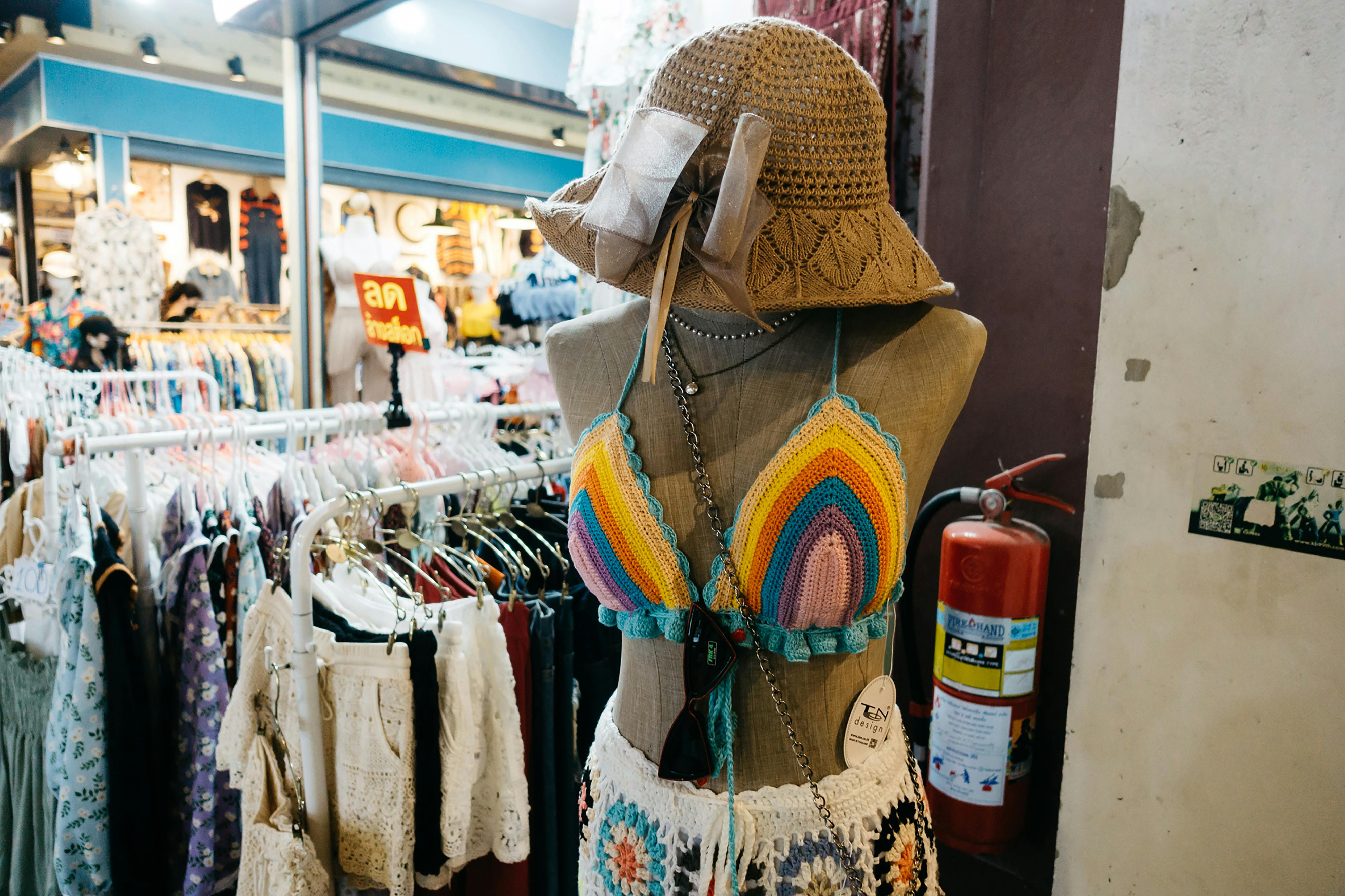 Vibrant crochet bikini and hat displayed on a mannequin in a lively indoor market.