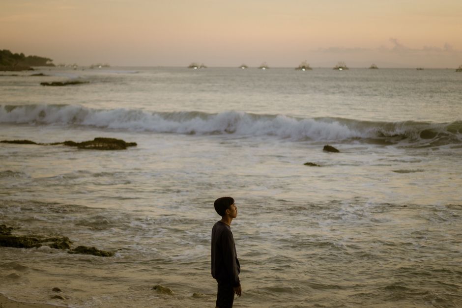 A young man stands at the Banten coast, gazing at the sunset over the sea. Tranquil and serene setting.