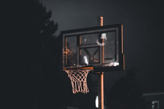 A basketball hoop lit up during the night, captured outdoors with a dark moody vibe.