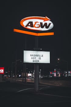 A well-lit A&W sign promoting Nashville hot chicken against a dark urban backdrop at night.