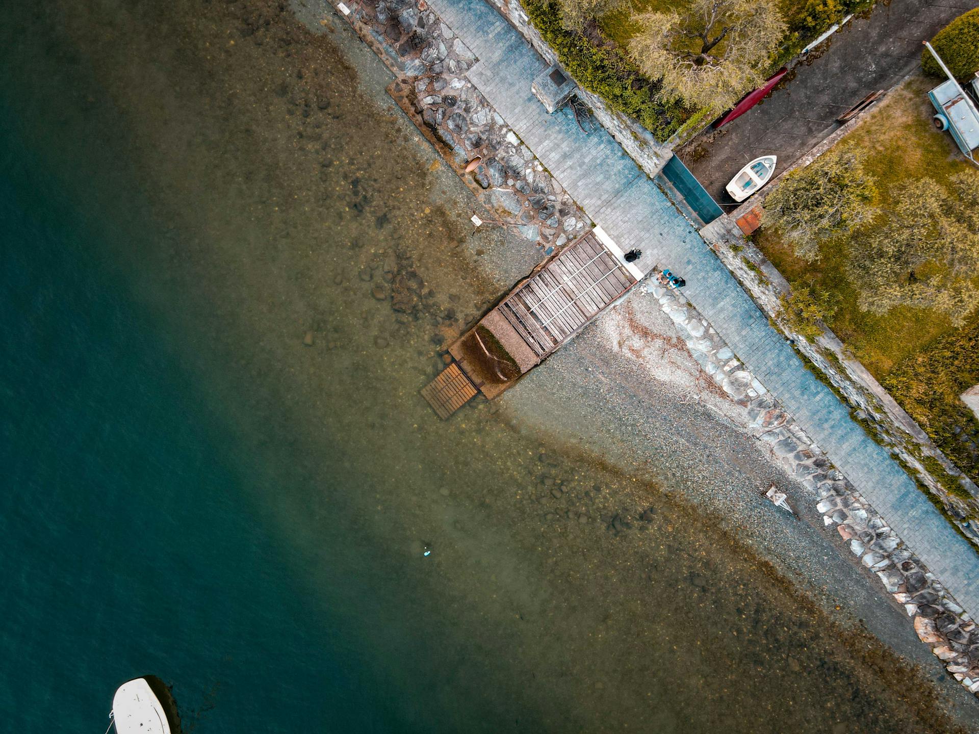 Aerial view of a serene coastal pier with a nearby boat and clear water.