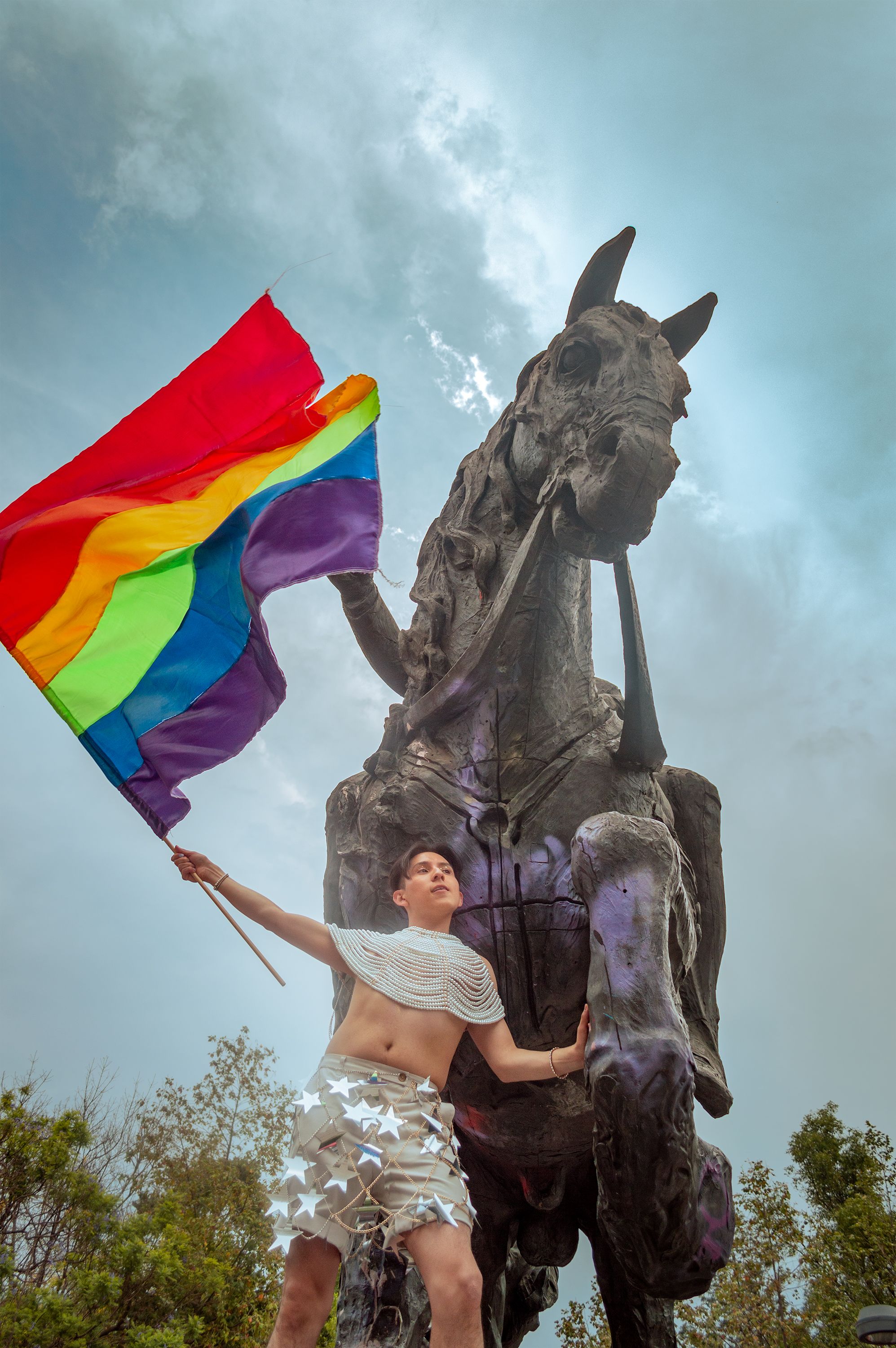 Low-angle shot of an individual with a pride flag next to a statue in México City.