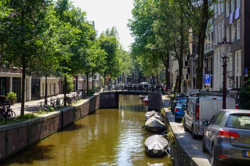 Free Sunny view of Amsterdam's iconic canal lined with trees, bikes, and boats, capturing the city's charm. Stock Photo
