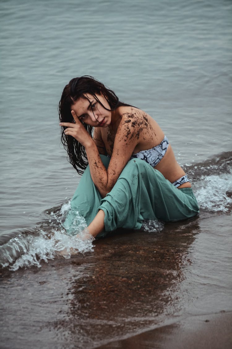 Woman Sitting On A Seashore With Her Arm Dirty From Wet Sand 