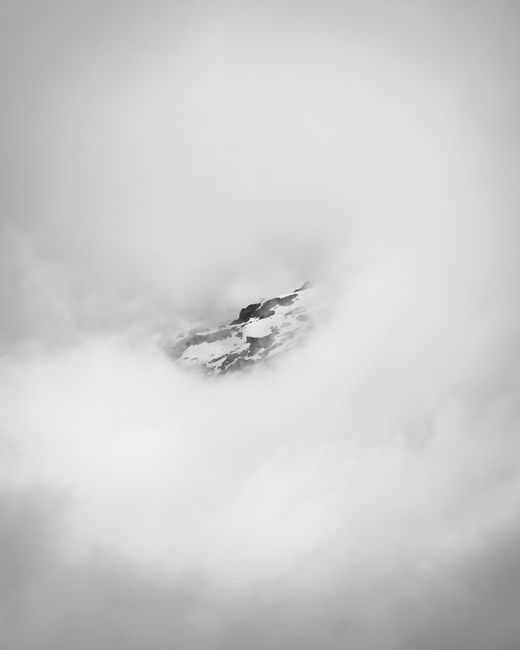 Dramatic black and white photo of a mountain peak enveloped in winter clouds in Tirol, Austria.