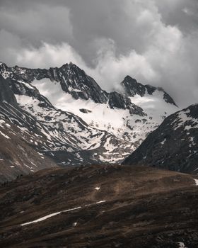 Snow-covered mountains under a cloudy sky in Tirol, Austria. Captures rugged winter beauty.