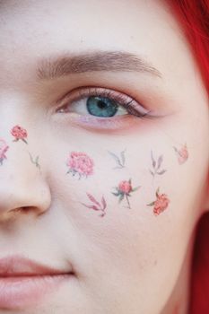 Intricate face art with floral designs on a woman's face with red hair and blue eyes.