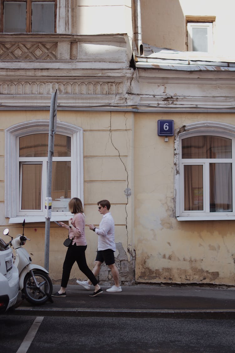 A Man And Woman Walking On The Sidewalk