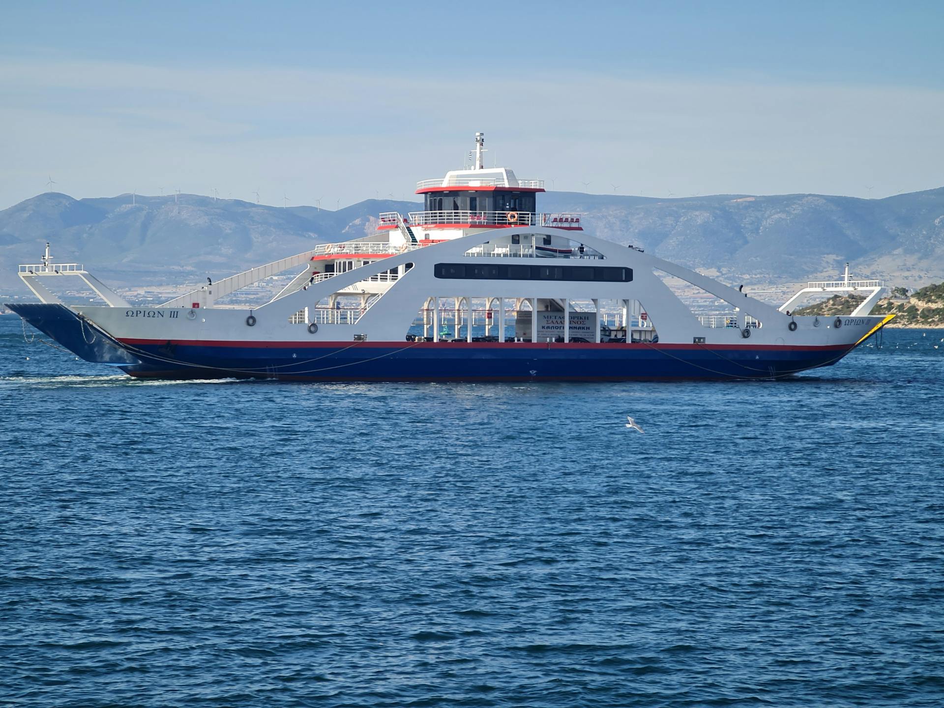 A modern ferry sailing through the beautiful waters of Greece with distant mountains in the background.