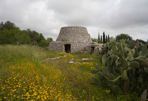Historic stone hut surrounded by flowers and cactus in Salve, Puglia.
