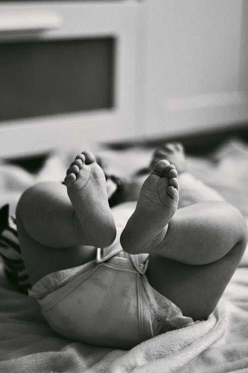 Free Feet of a Baby Lying on a Bed in Black and White Stock Photo