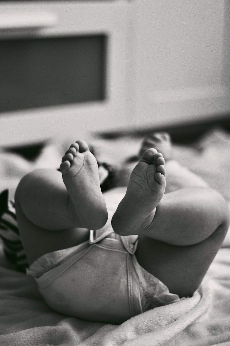 Feet Of A Baby Lying On A Bed In Black And White