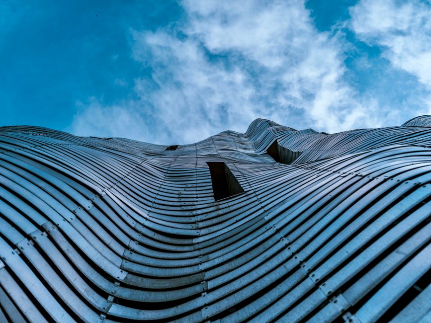Architectural abstract of a wavy steel structure against a vibrant blue sky, showcasing modern design. Architectural abstract of a wavy steel structure against a vibrant blue sky, showcasing modern design.